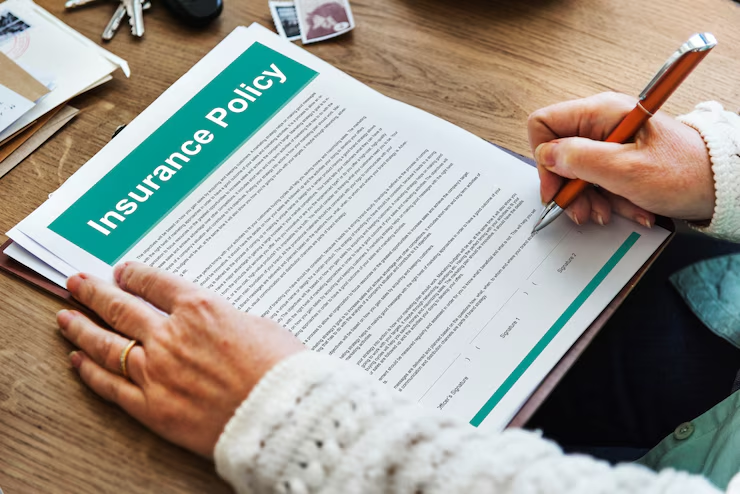 "Person signing an insurance policy document at a desk, with keys and papers nearby."