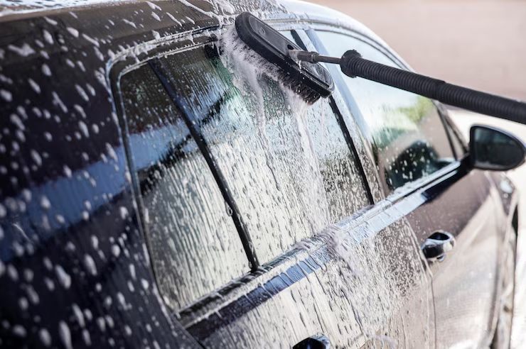 "Close-up of a black car being washed with a brush and soapy water, focusing on the side windows and door."