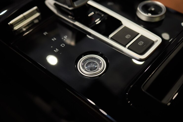Close-up of a modern car’s center console featuring a gear selector, electronic parking brake buttons, and a start/stop ignition button with a sleek black and chrome design.