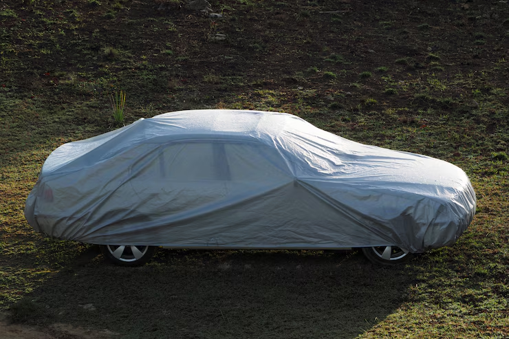 Car fully covered with a protective gray cover, parked on a grassy area.