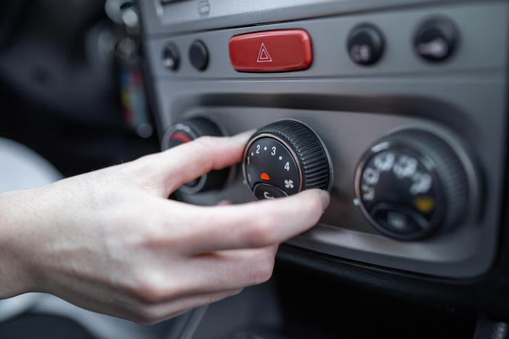 A close-up of a hand adjusting the fan speed dial on a car's climate control panel, with other temperature and air direction knobs visible.