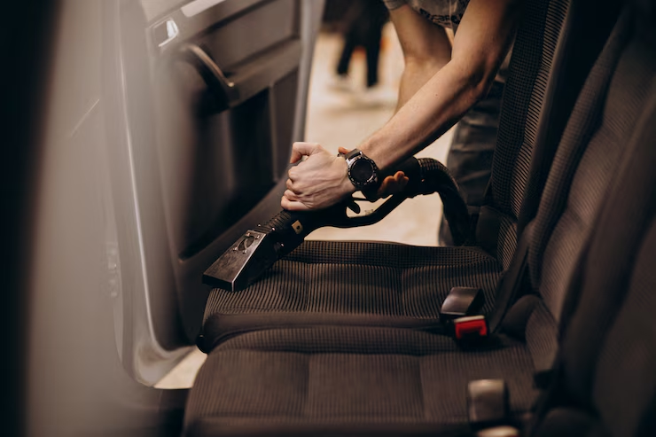 "Person using a professional vacuum extractor to clean the fabric seats inside a car, focusing on automotive interior detailing."